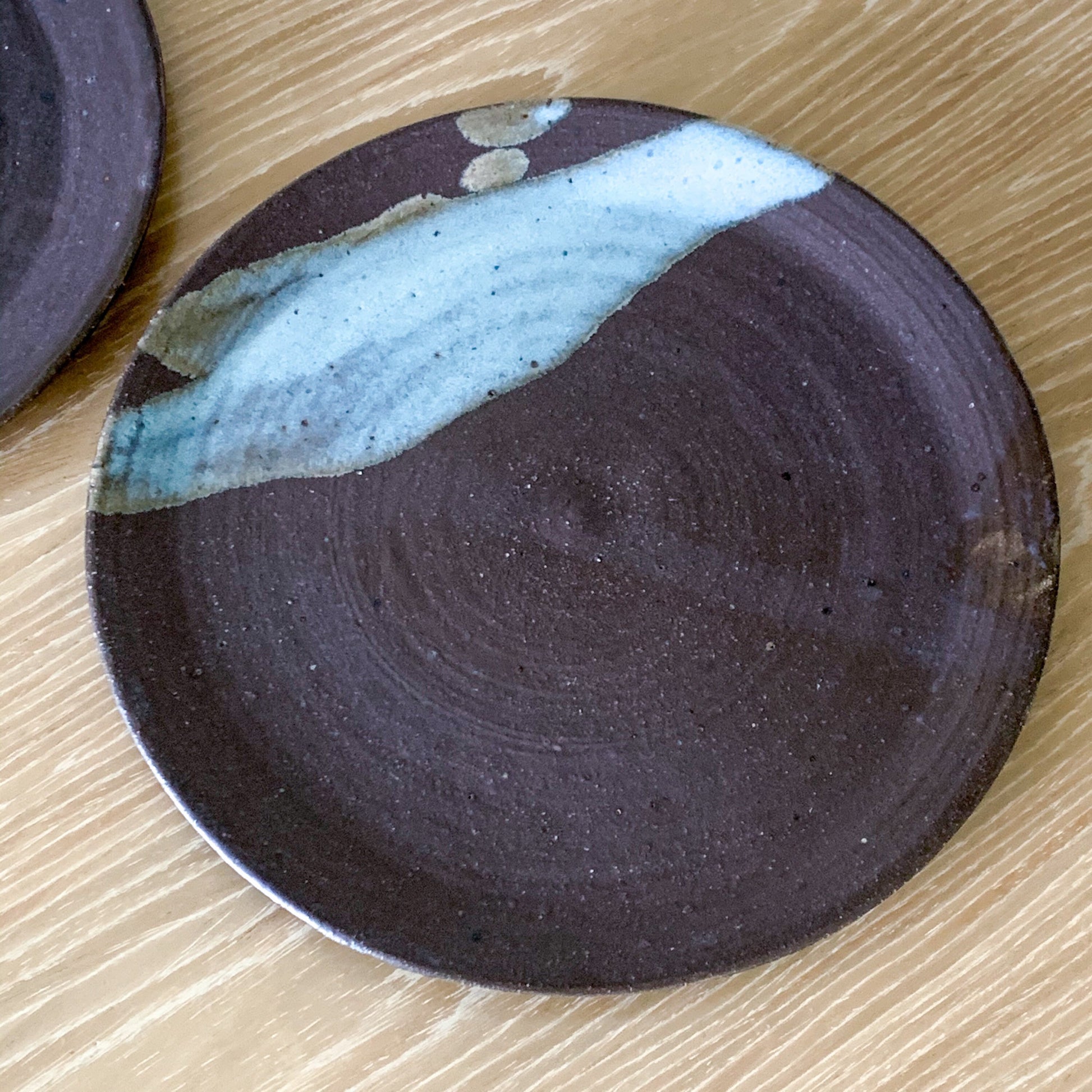 Pottery plate in matt brown color with shiny blue splash